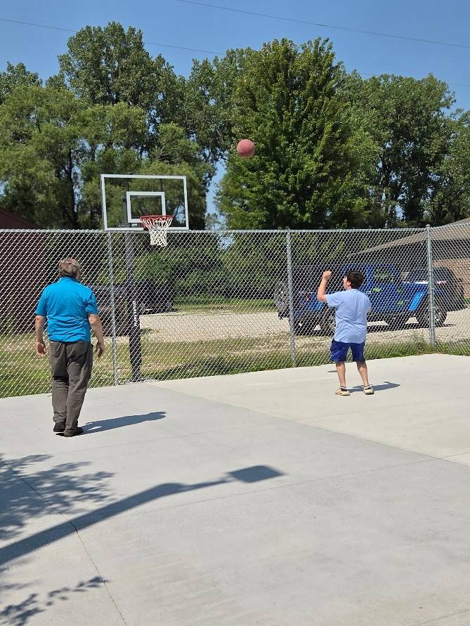 Two boys and a volunteer shooting hoops on the newly renovated Young House basketball court